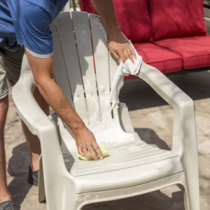 Homeowner cleaning faded plastic patio furniture chair before restoring its color.