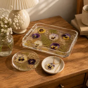 A pressed flower resin tray styled alongside a matching coaster and pendant on a bedside table.